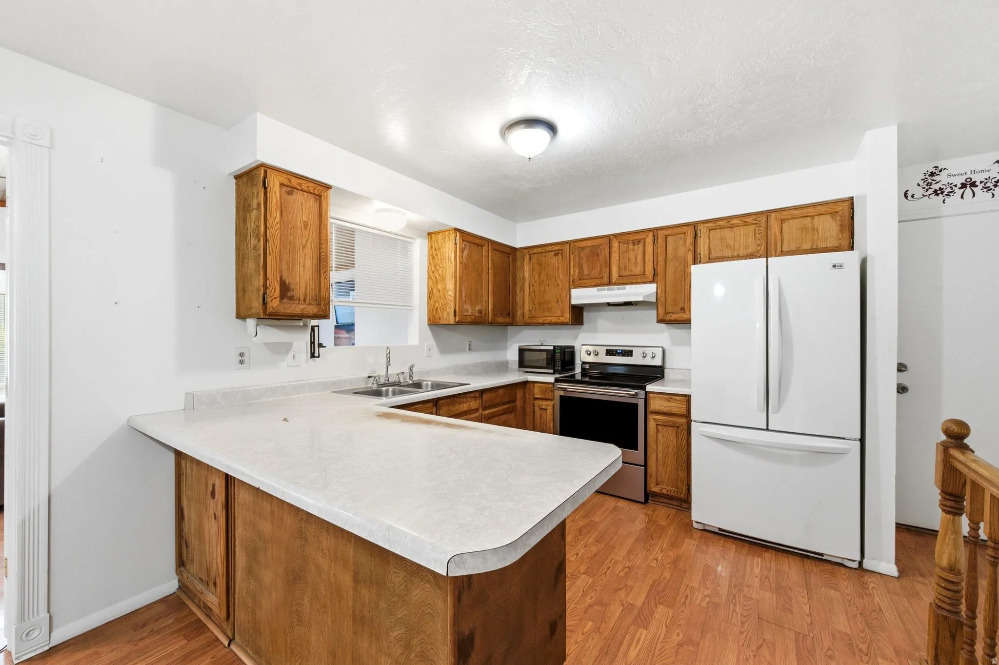 Kitchen with wood finish cabinets, a peninsula, freestanding refrigerator, and light wood finished floors
