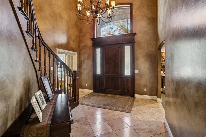 Tiled entryway featuring a high ceiling, arched walkways, a chandelier, and stairway
