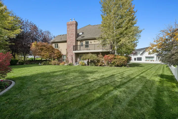 Rear view of house with a yard, a chimney, stucco siding, and a shingled roof