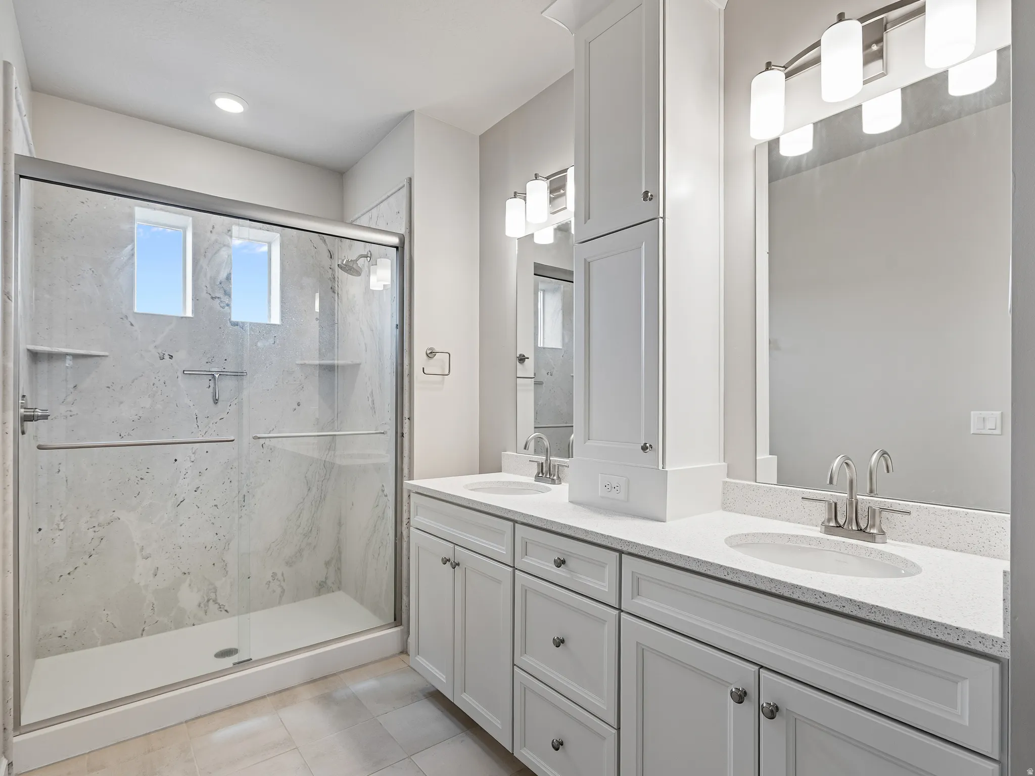 Bathroom with double vanity, a marble finish shower, and light tile patterned flooring