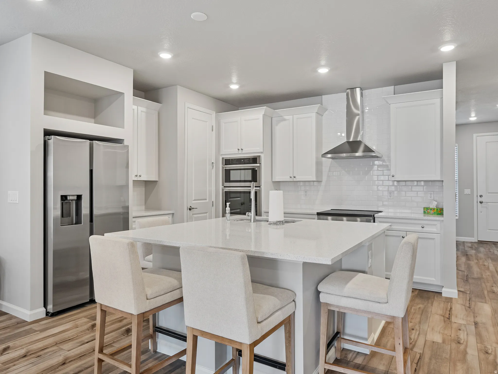 Kitchen with stainless steel appliances, white cabinetry, light wood-type flooring, recessed lighting, and an island with sink