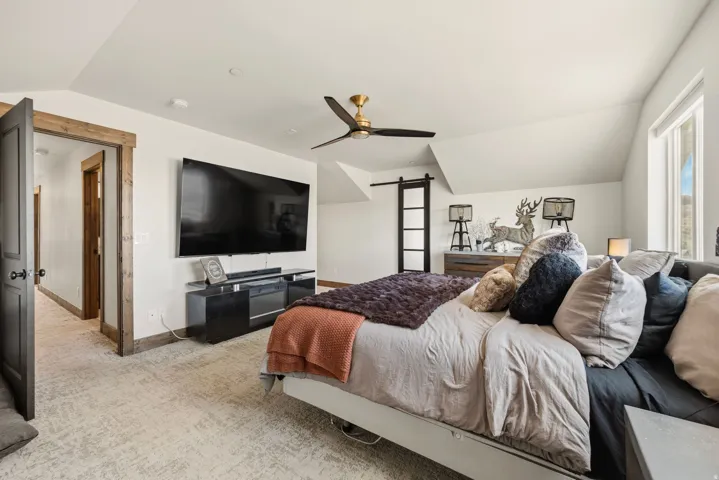 Bedroom with vaulted ceiling, a barn door, light colored carpet, and ceiling fan