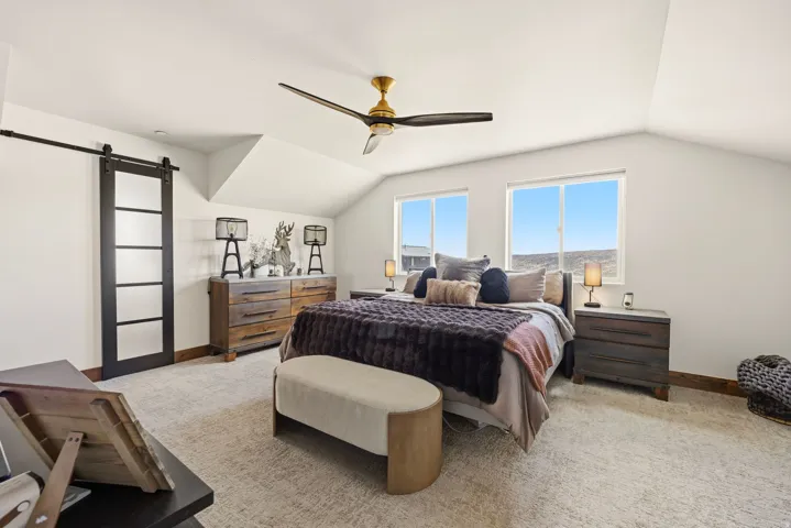 Bedroom with a barn door, light colored carpet, lofted ceiling, and a ceiling fan