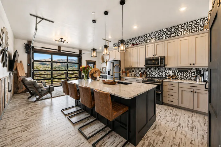Dual tone kitchen featuring a kitchen bar, light stone counters, a center island with sink, stainless steel appliances, and hanging light fixtures