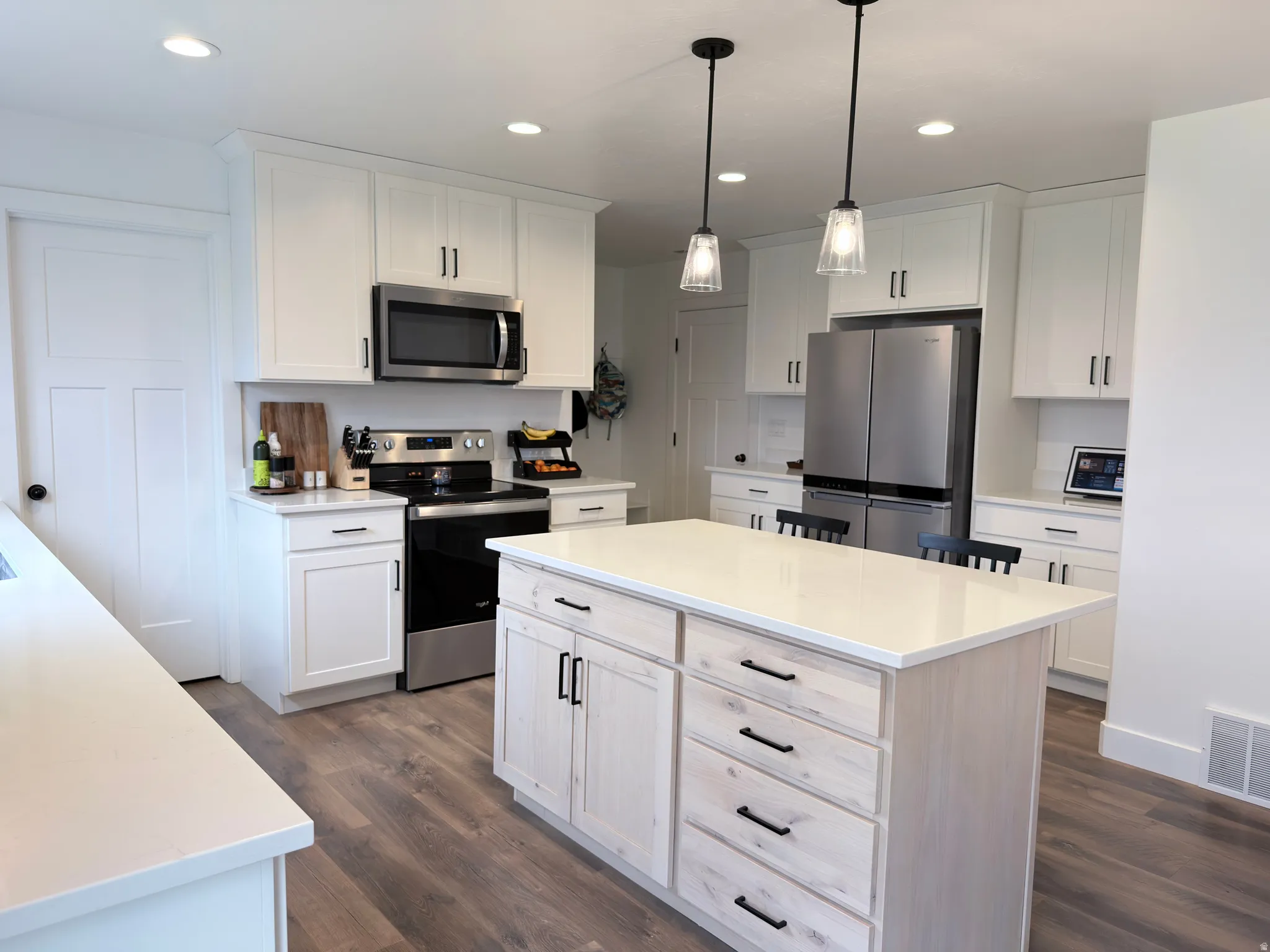 Kitchen featuring stainless steel appliances, a kitchen island, dark wood-style floors, and white cabinetry