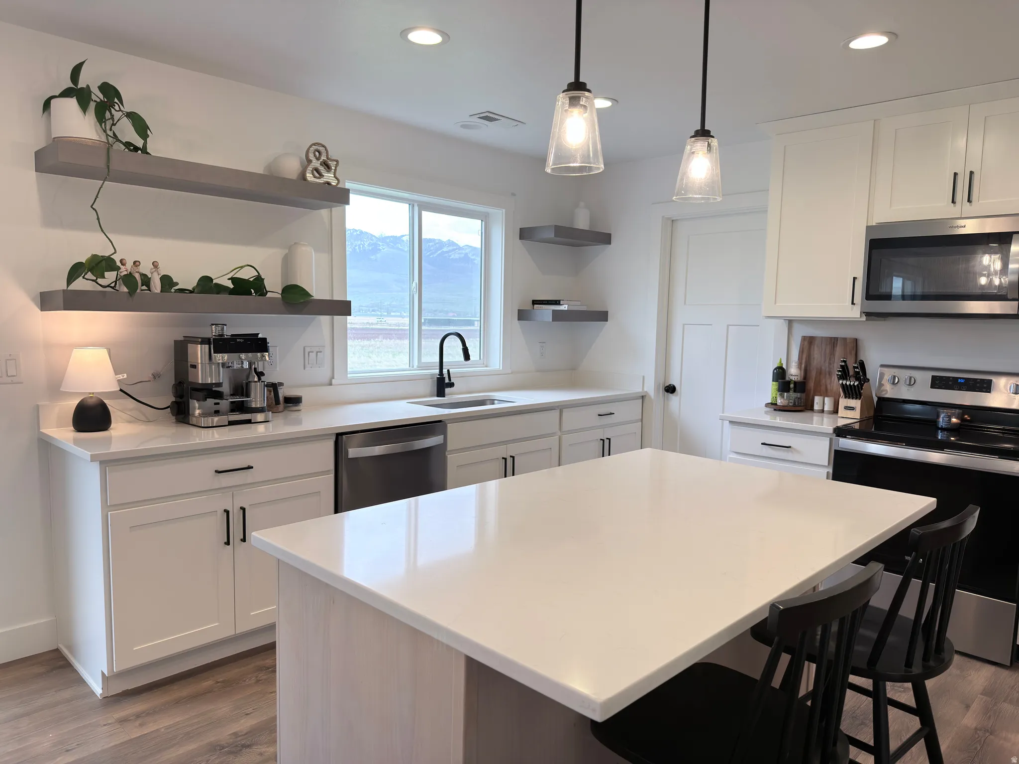 Kitchen featuring stainless steel appliances, white cabinets, open shelves, dark wood finished floors, and a kitchen bar