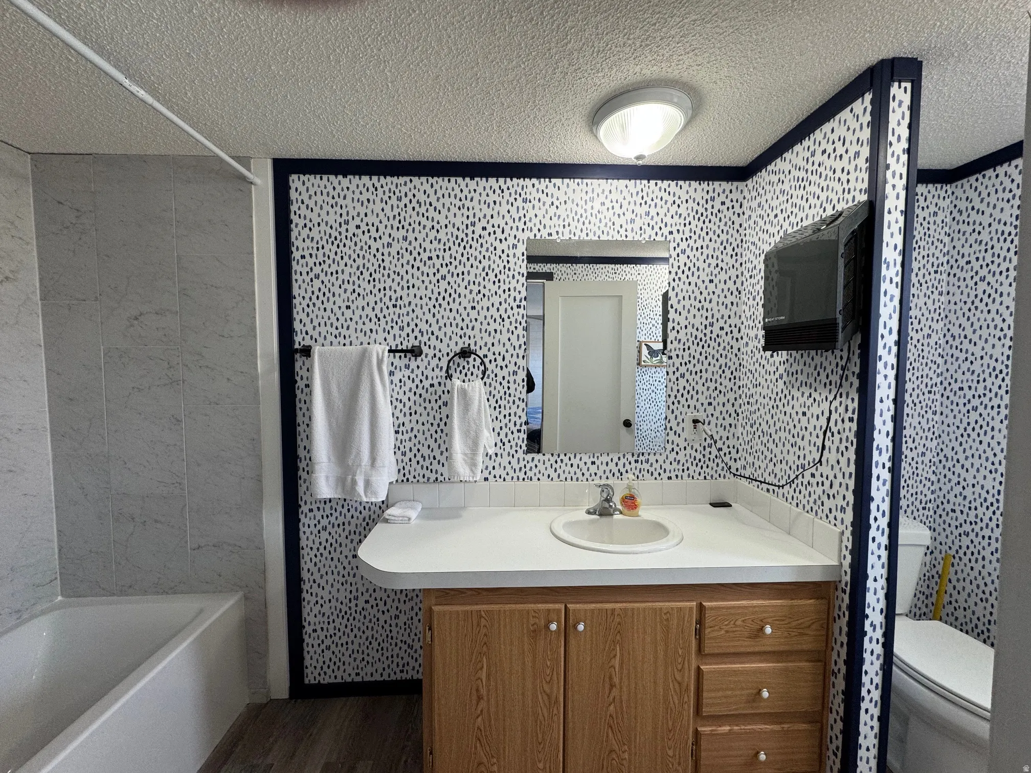 Bathroom featuring vanity,  shower combination, a textured ceiling, tile walls, and dark wood finished floors
