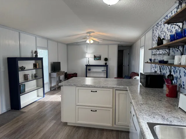 Kitchen with a peninsula, open shelves, light countertops, black microwave, and ceiling fan