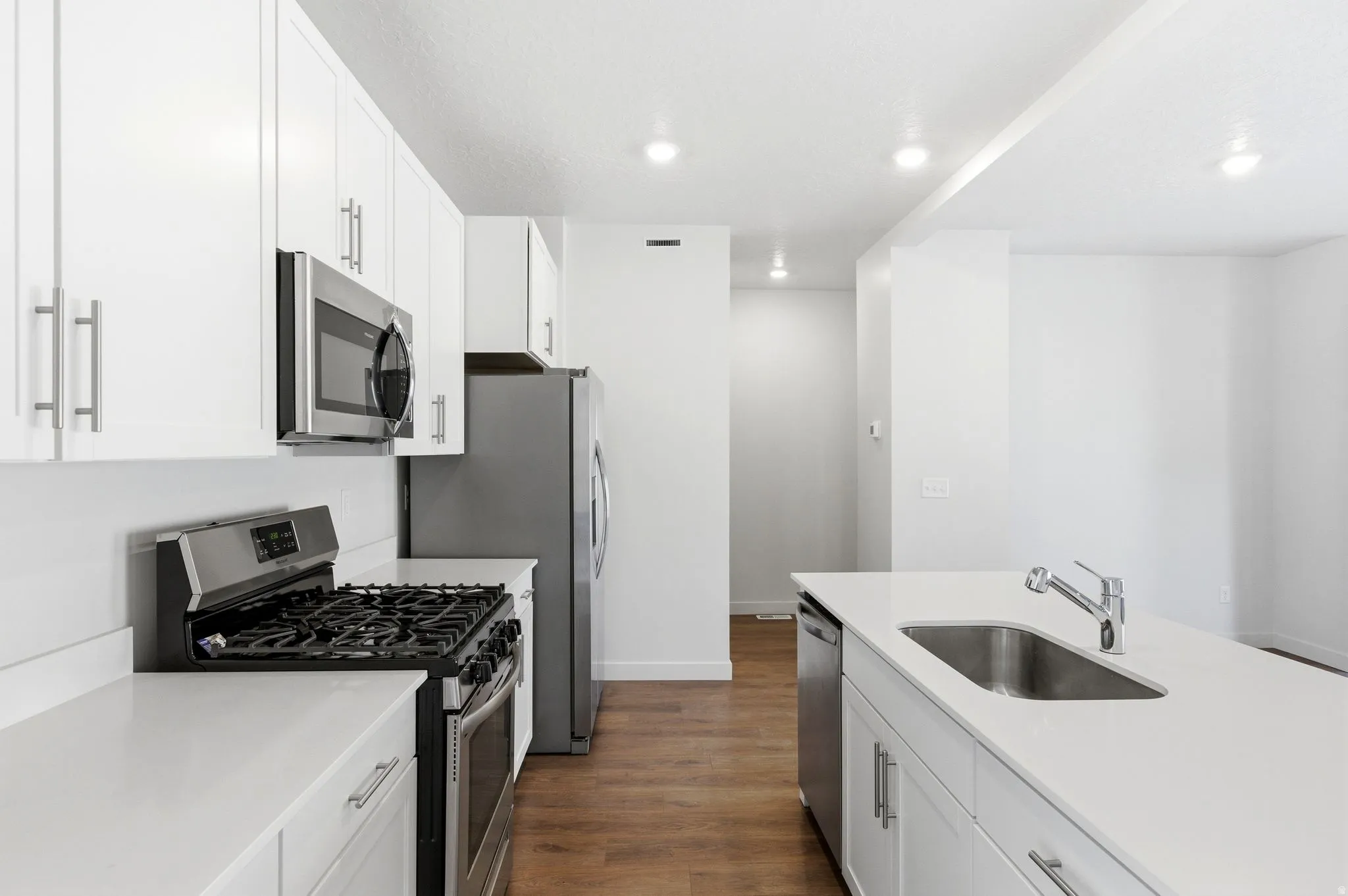 Kitchen with stainless steel appliances, white cabinets, dark wood-type flooring, recessed lighting, and light stone counters