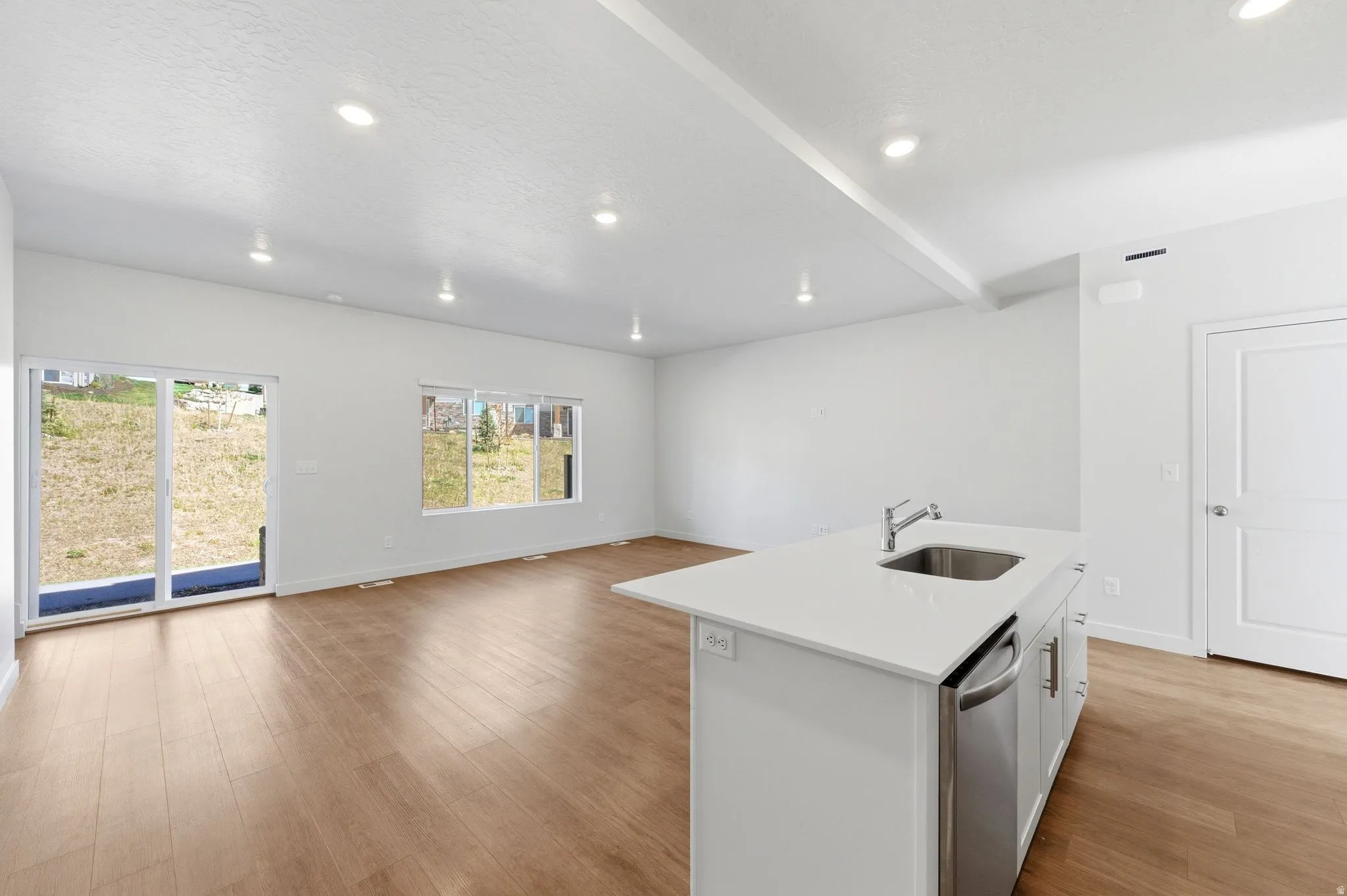 Kitchen featuring an island with sink, open floor plan, white cabinetry, light wood-style floors, and light stone counters