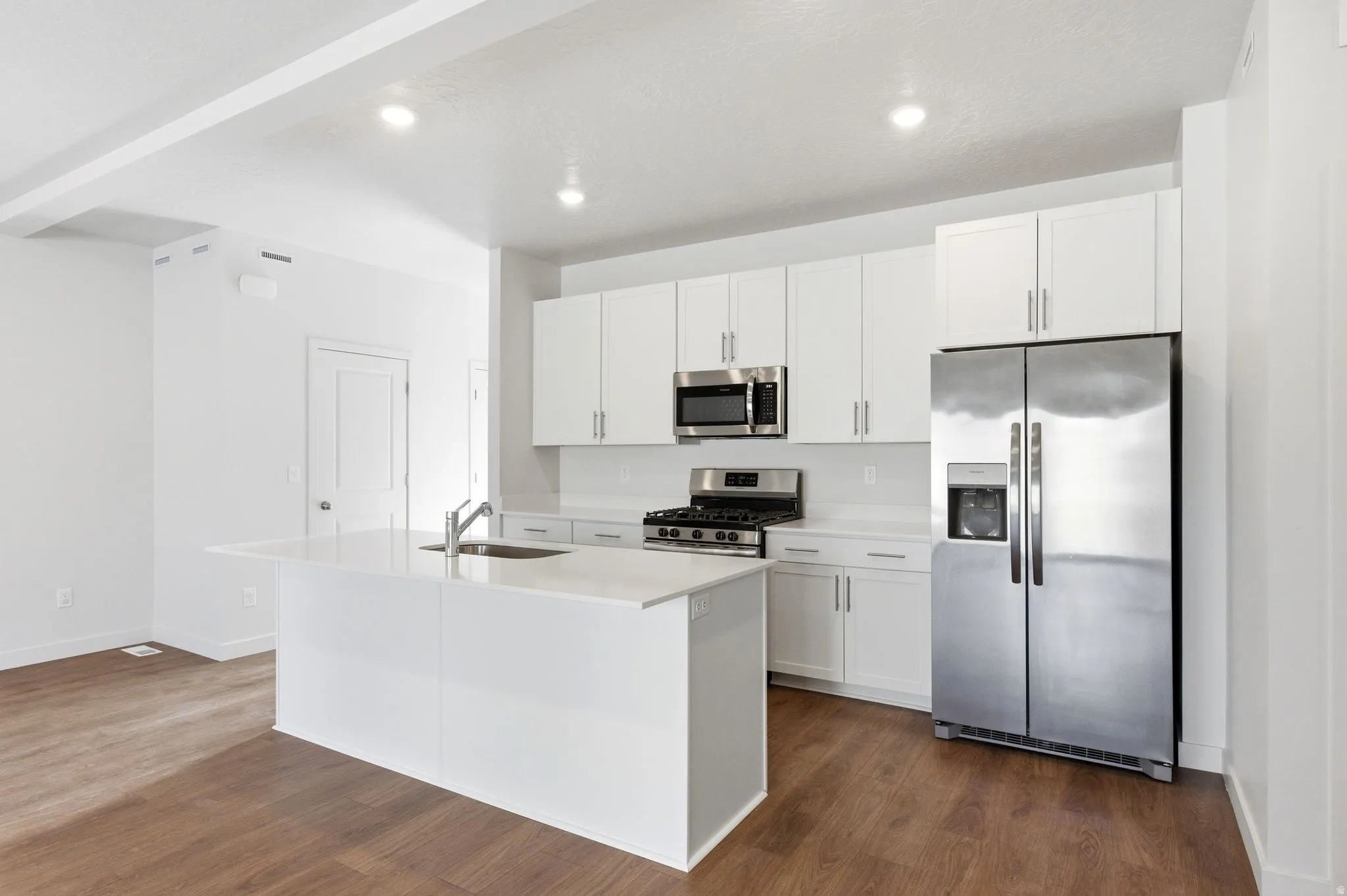 Kitchen with stainless steel appliances, dark wood-style flooring, a center island with sink, white cabinets, and recessed lighting