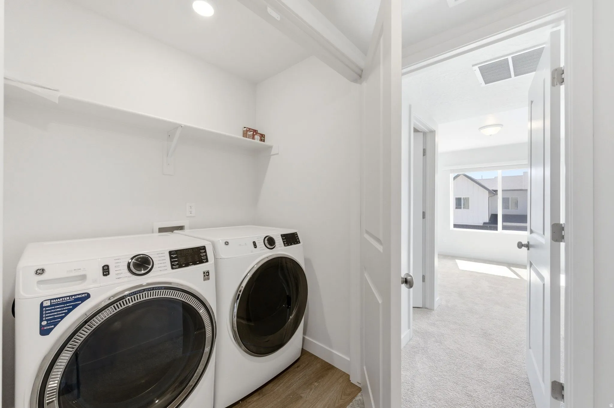 Laundry area with washer and clothes dryer, light colored carpet, and light wood finished floors