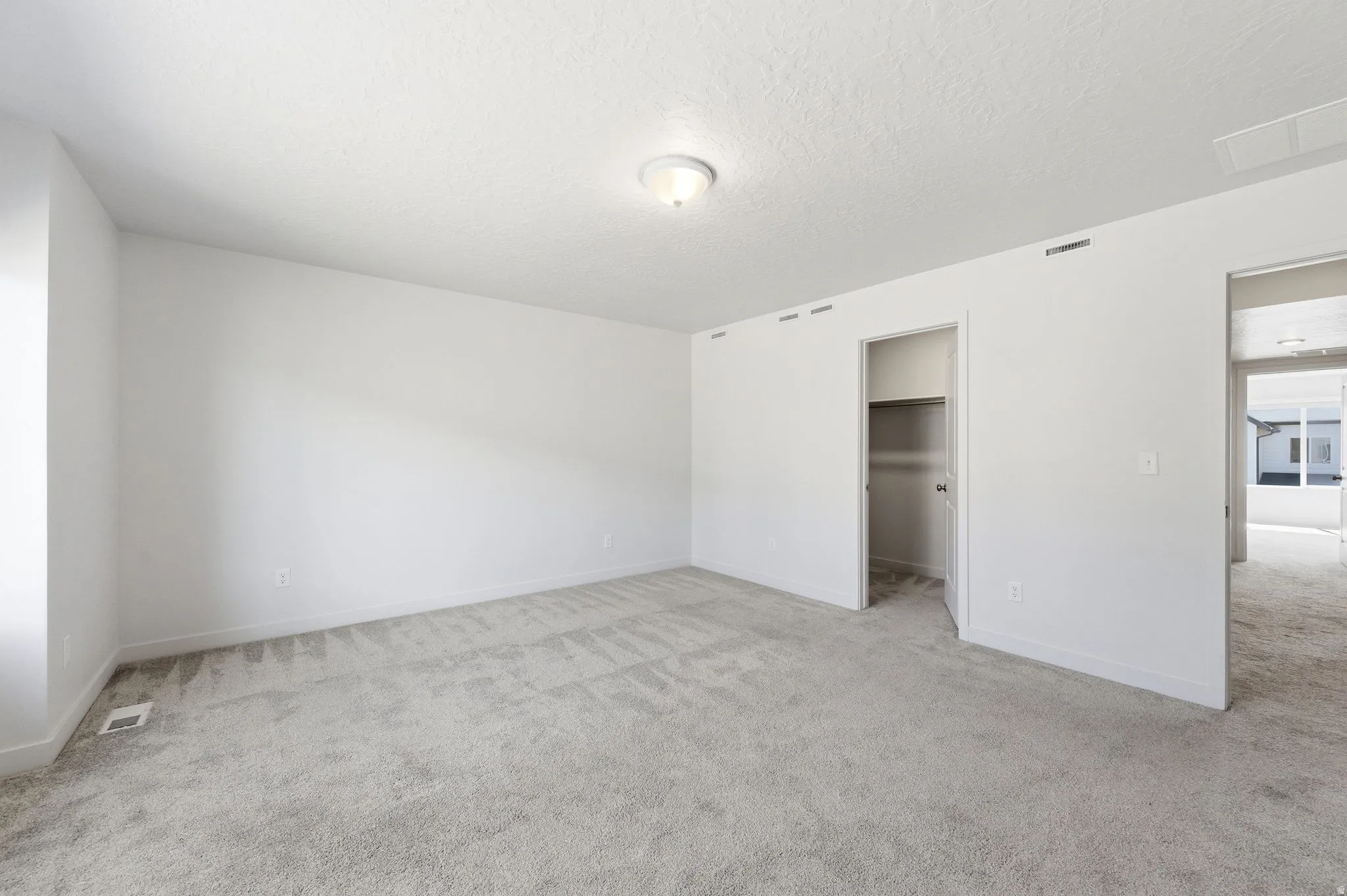 Unfurnished bedroom with light colored carpet, a walk in closet, and a textured ceiling