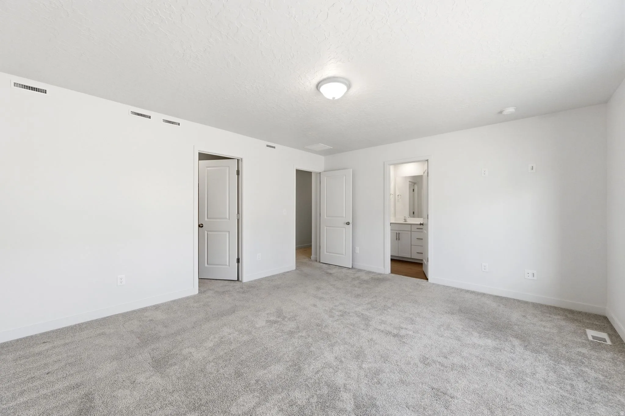 Unfurnished bedroom with carpet, ensuite bathroom, and a textured ceiling