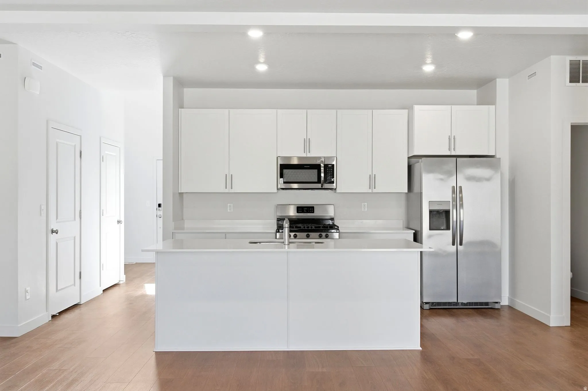 Kitchen featuring stainless steel appliances, white cabinetry, light wood-style flooring, a kitchen island with sink, and light stone countertops