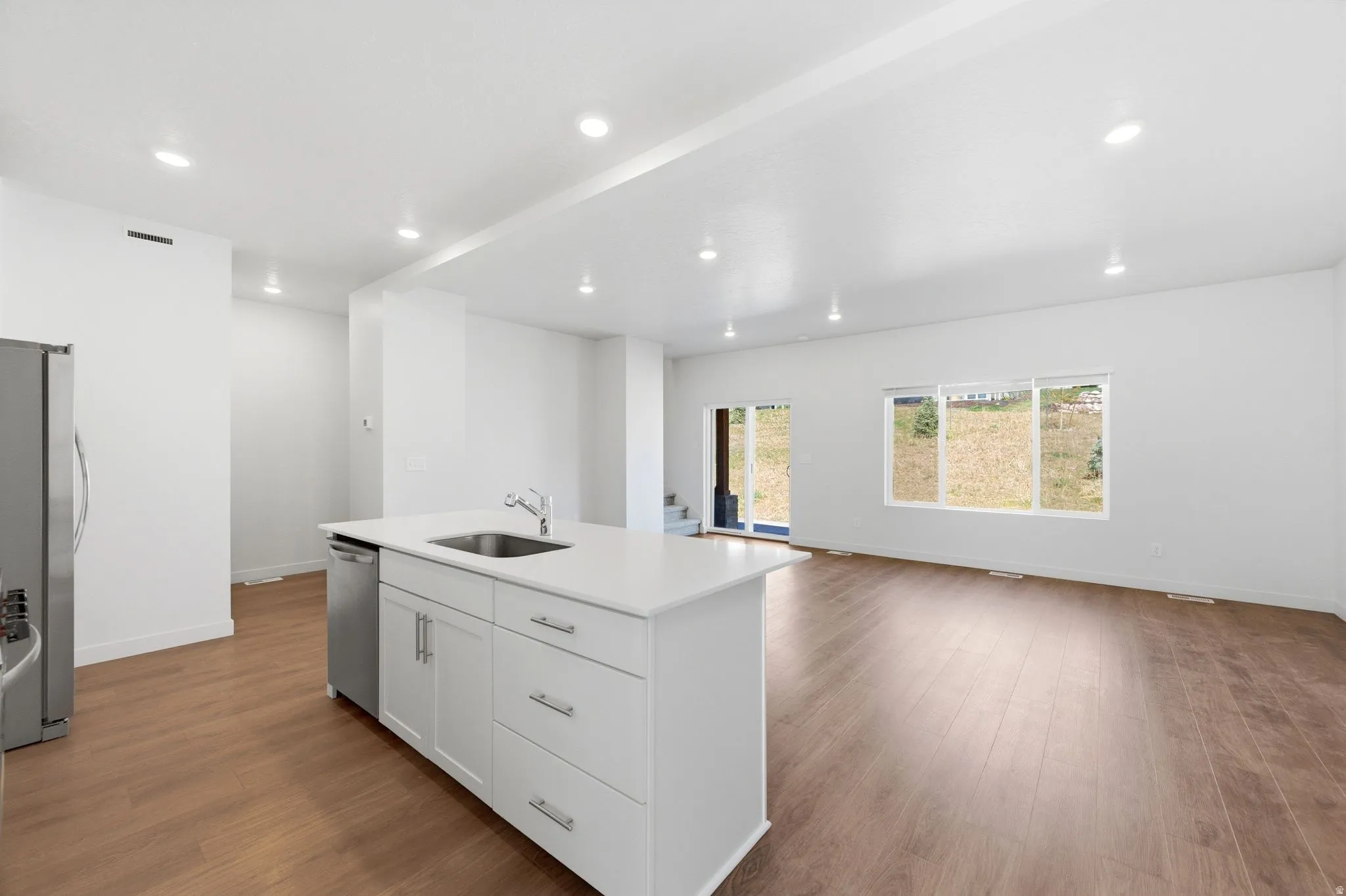 Kitchen featuring open floor plan, a kitchen island with sink, dark wood-style flooring, white cabinets, and recessed lighting