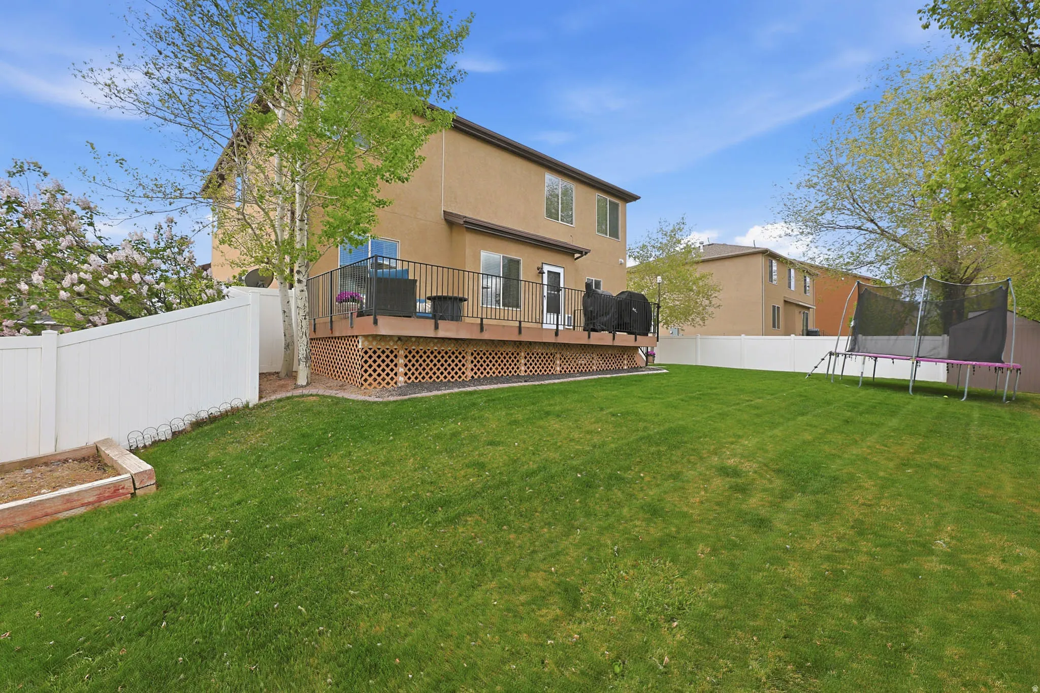 Back of property featuring stucco siding, a deck, a fenced backyard, and a trampoline