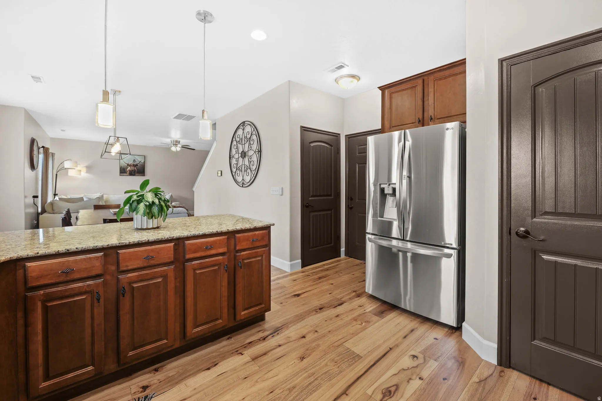 Kitchen with stainless steel fridge, light stone countertops, hardwood finished floors, hanging light fixtures, and open floor plan