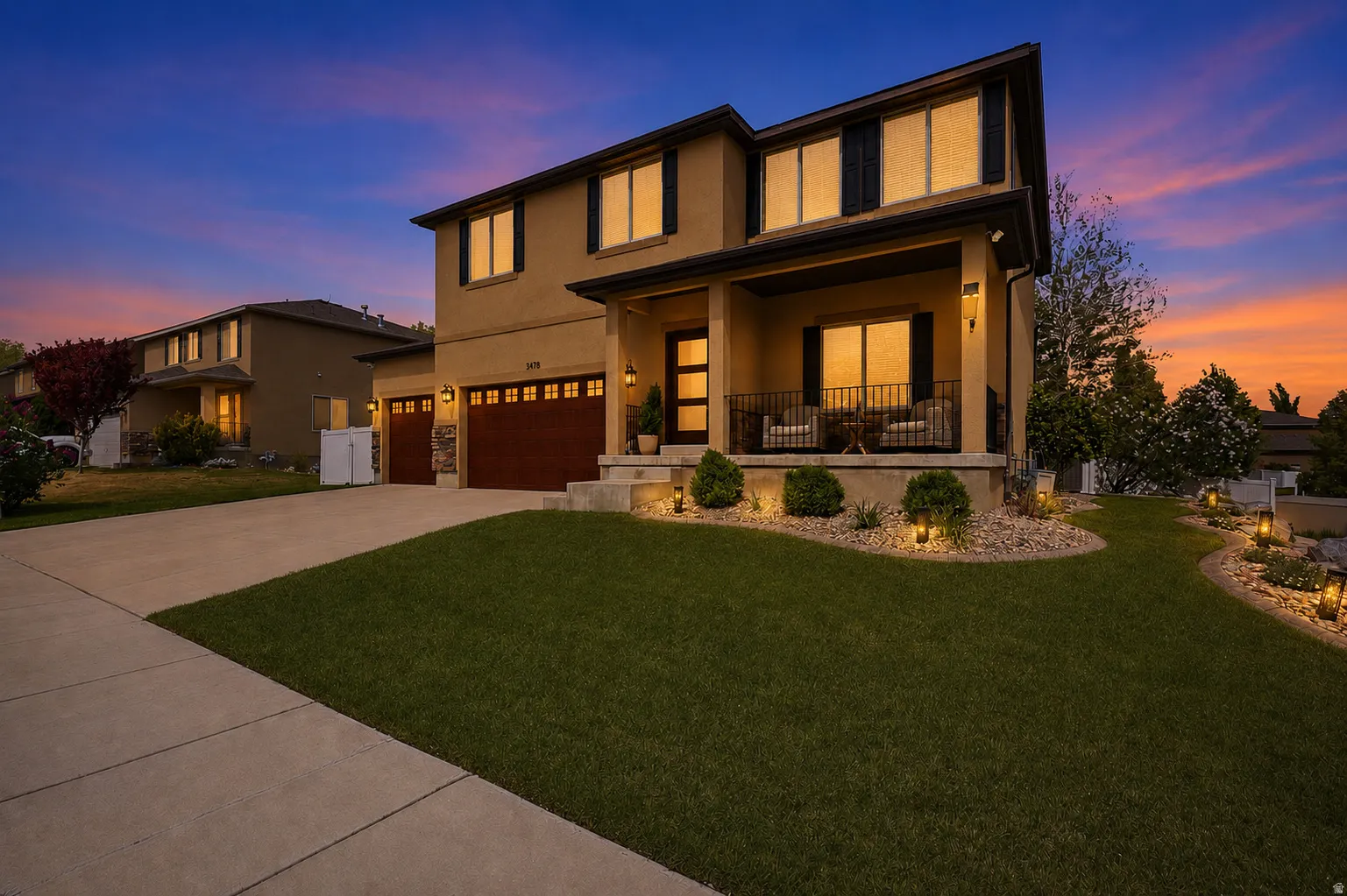 Stucco exterior with a covered porch featuring dark railings, a prominent front door with vertical glass inserts, and two attached garage doors with decorative windows
