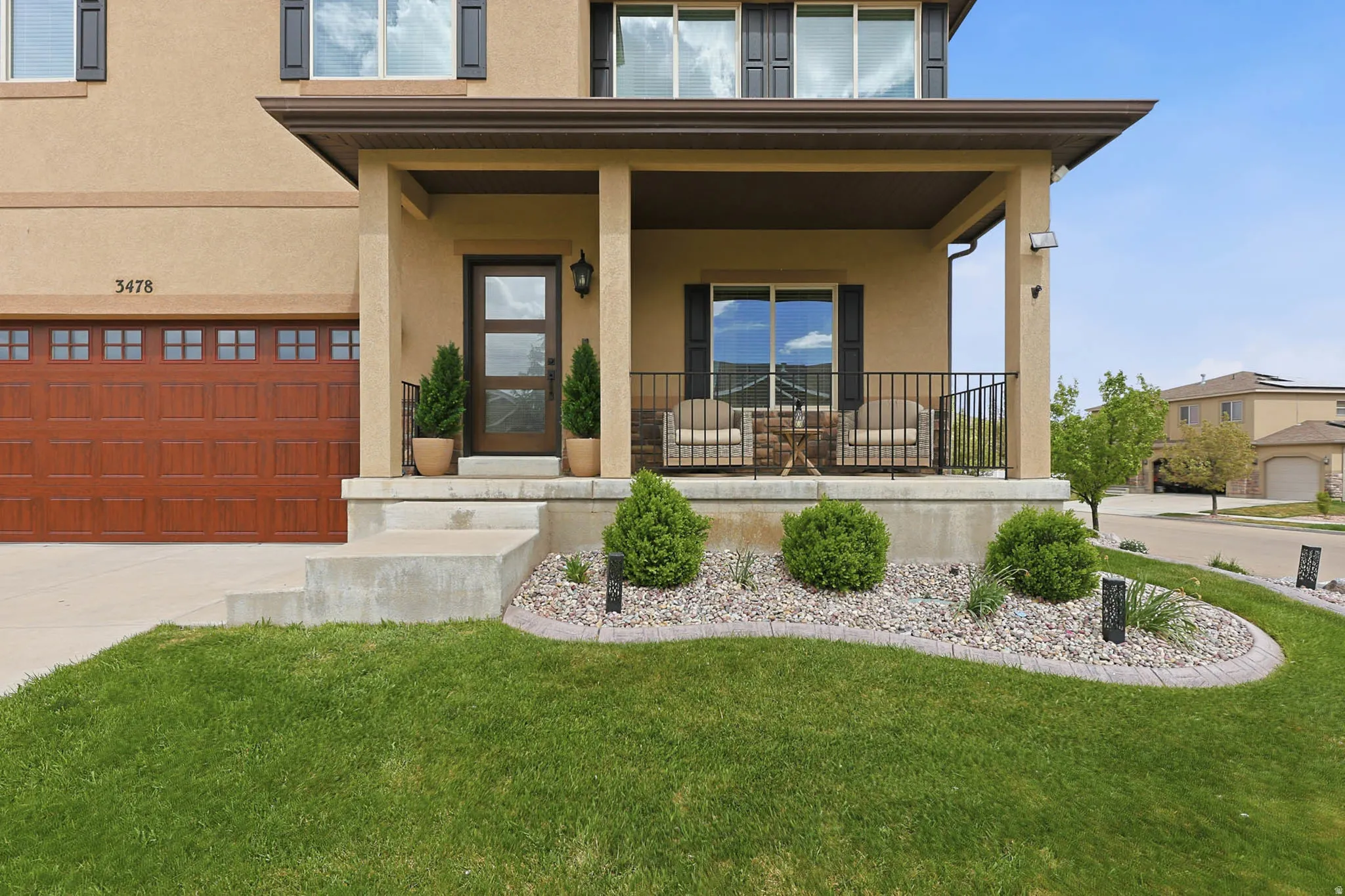 View of front of home with stucco siding, covered porch, a professionally landscaped front yard, a 3 car garage, and concrete driveway