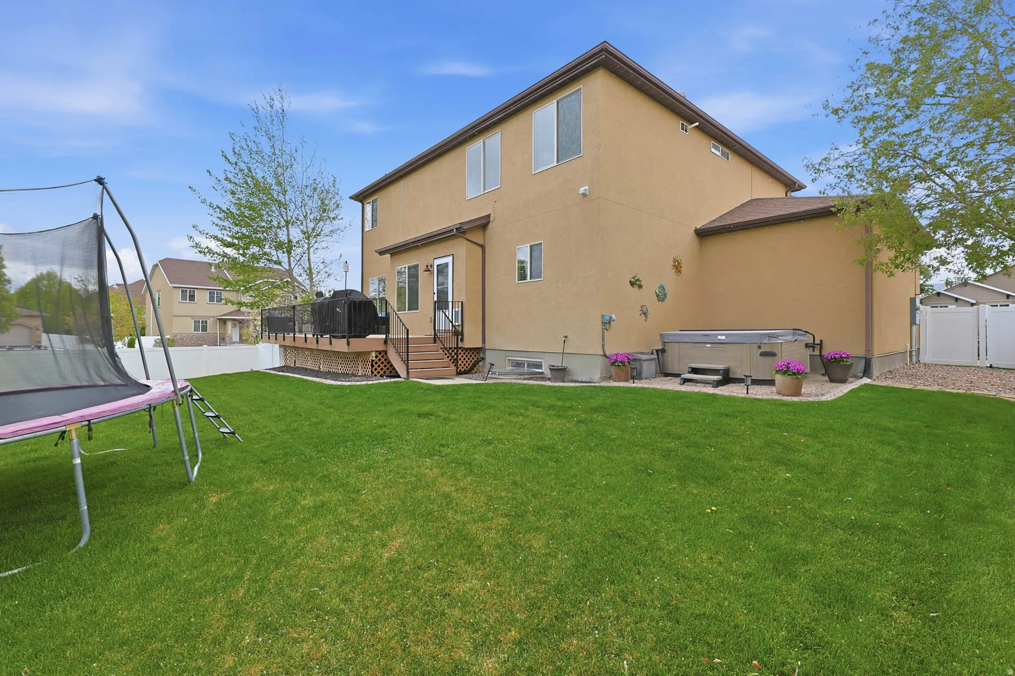 Back of property with a trampoline, a hot tub, a fenced backyard, a wooden deck, and stucco siding