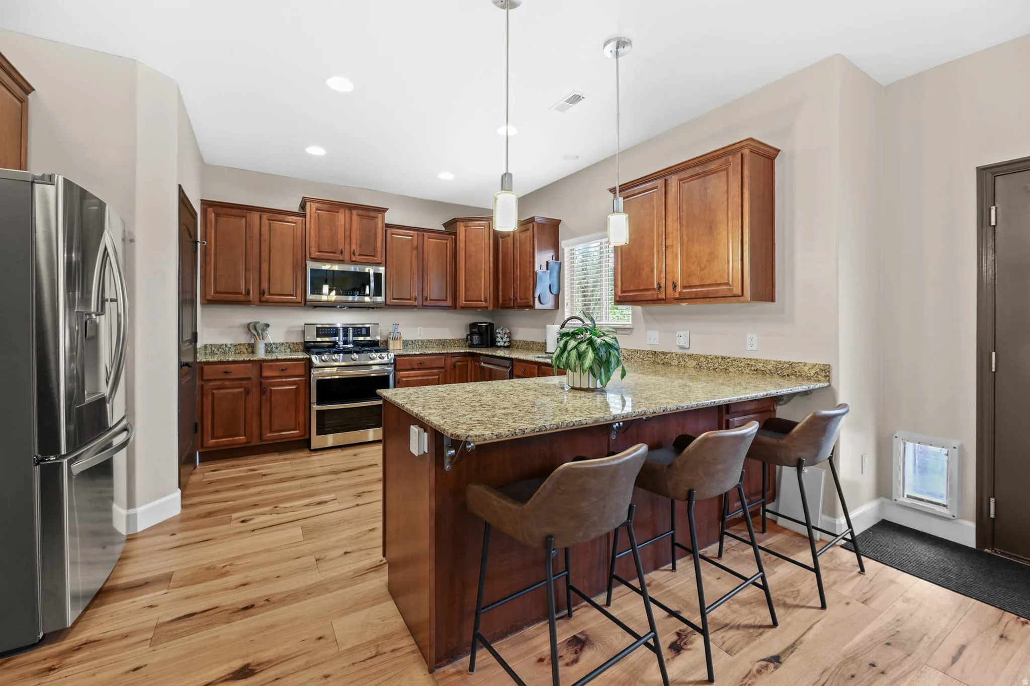 Kitchen featuring stainless steel appliances, wood cabinetry, a breakfast bar, engineered hardwood flooring, and light stone countertops