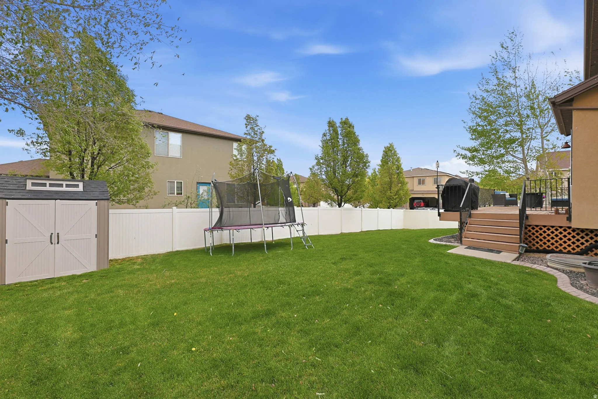 Fenced backyard with a trampoline, a storage unit, and a wooden deck