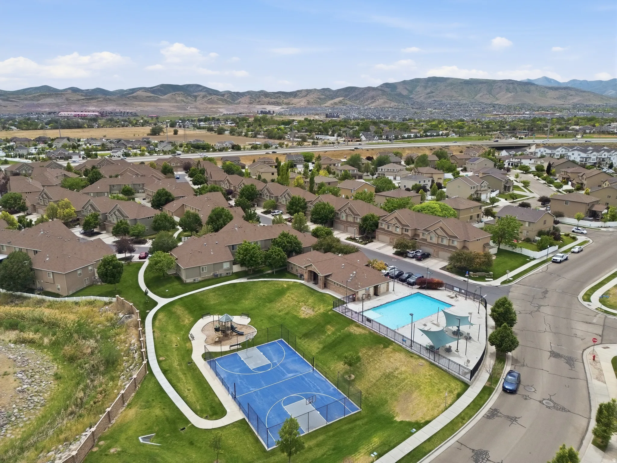Community amenities including a swimming pool with shade structures, a sports court, and a playground within a landscaped park area