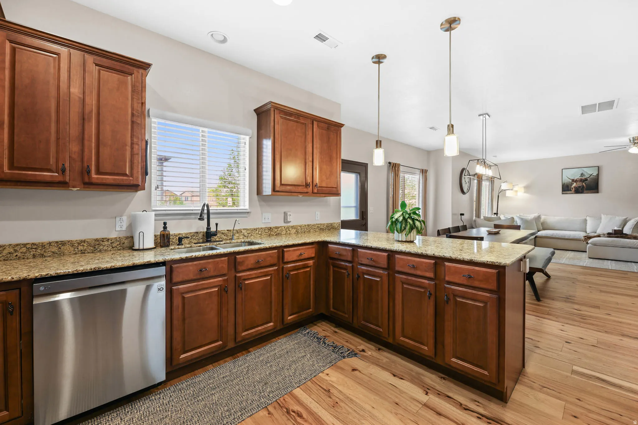 Kitchen with dishwasher, light stone countertops, open floor plan, pendant lighting, and engineered hardwood flooring