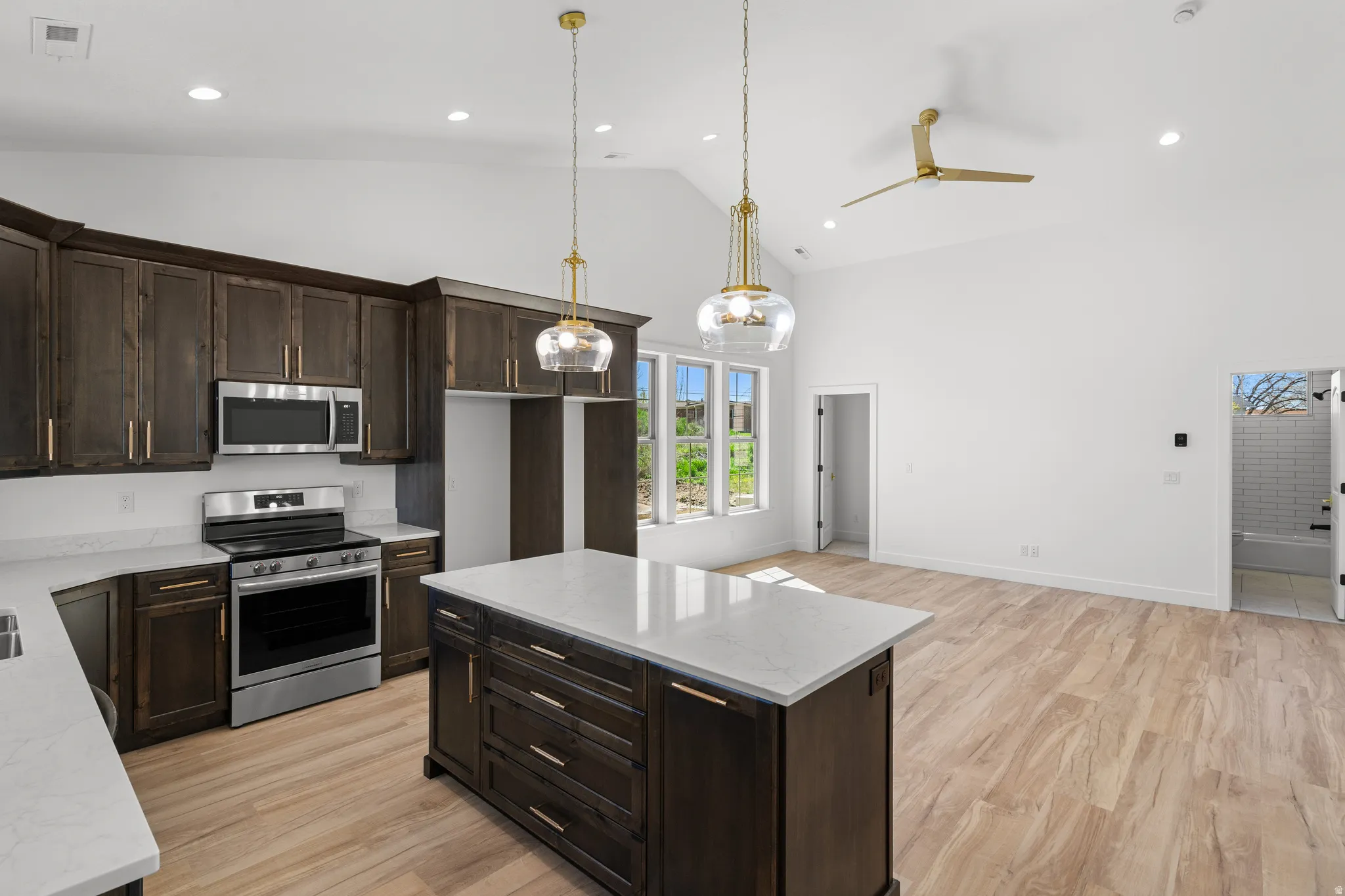 Kitchen with dark wood finish cabinetry, stainless steel appliances, light wood-type flooring, light stone countertops, and vaulted ceiling