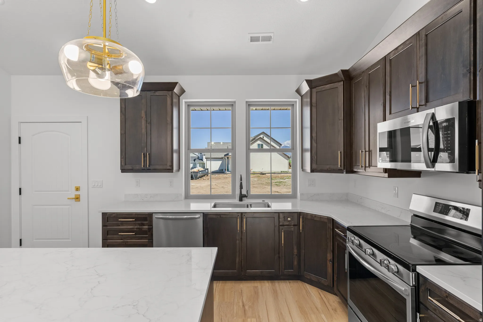 Kitchen featuring dark wood finish cabinets, stainless steel appliances, light wood finished floors, pendant lighting, and light stone counters