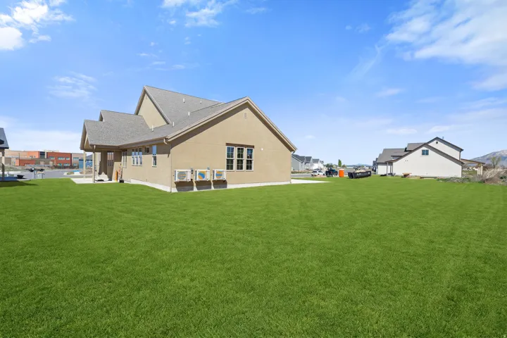 Rear view of house featuring a yard, stucco siding, and roof with shingles