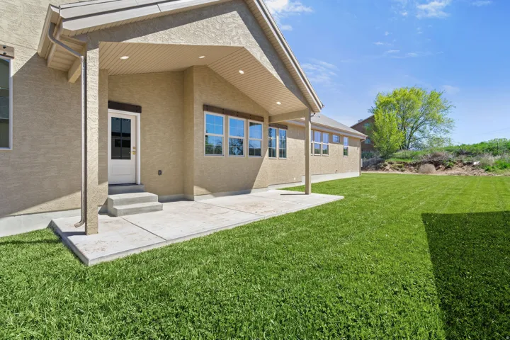Rear view of property featuring a lawn, stucco siding, a patio area, and entry steps