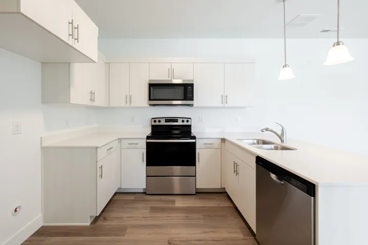 Kitchen featuring white cabinetry, stainless steel appliances, light-toned countertops, wood-finish flooring, and pendant lighting