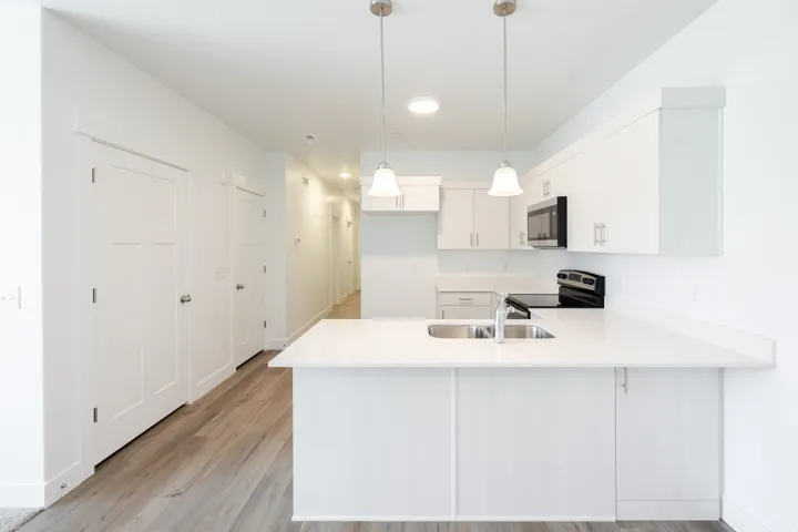 Kitchen island with a double basin sink, white cabinetry, integrated stainless steel microwave, and wood-finish flooring