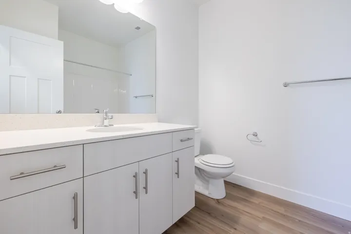 Bathroom featuring a single vanity with stone-finish countertop, undermount sink, wood-finish flooring, and white walls