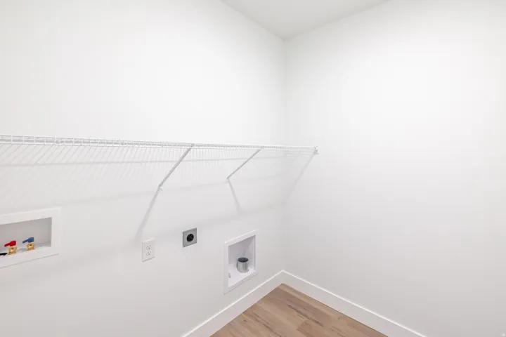 Laundry area featuring wood-finish flooring, white walls, and a wire shelf for storage