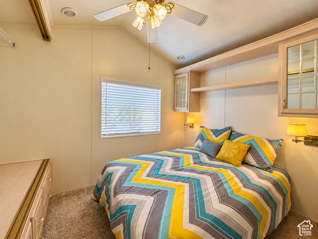 Vaulted ceiling with integrated lighting, built-in overhead cabinetry featuring glass-paneled doors, wall-mounted light fixtures, and window with horizontal blinds