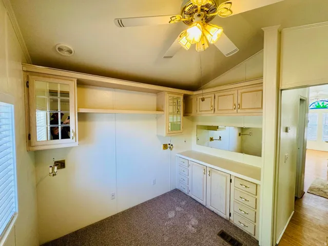 Laundry area with ceiling fan, vaulted ceiling, and dark colored carpet
