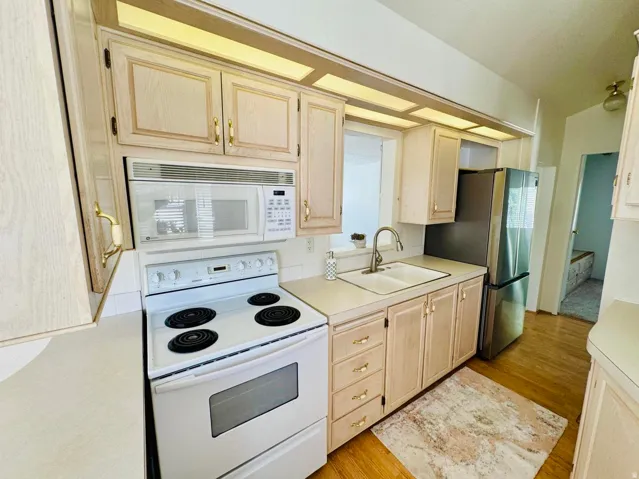 Kitchen with white appliances, light countertops, light wood finish cabinetry, light wood-type flooring, and lofted ceiling