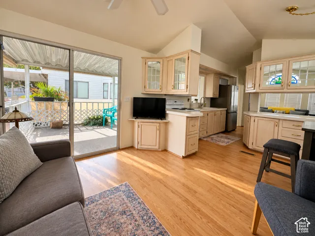 Living area featuring wood-finish flooring, vaulted ceilings, light-tone cabinetry with glass-front accents, and a sliding glass door providing external access to a covered patio