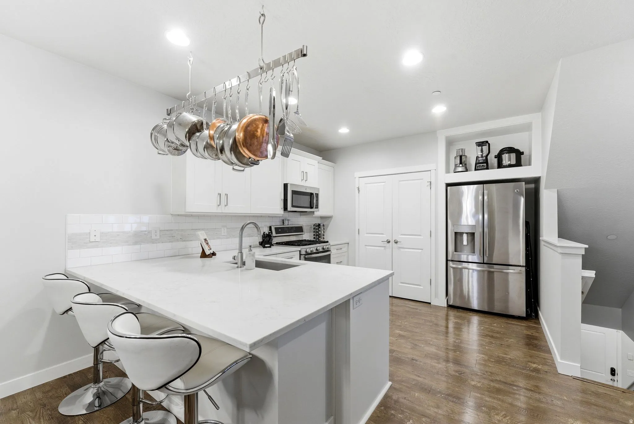 Kitchen with a breakfast bar area, stainless steel appliances, a peninsula, white cabinetry, and dark wood-style flooring