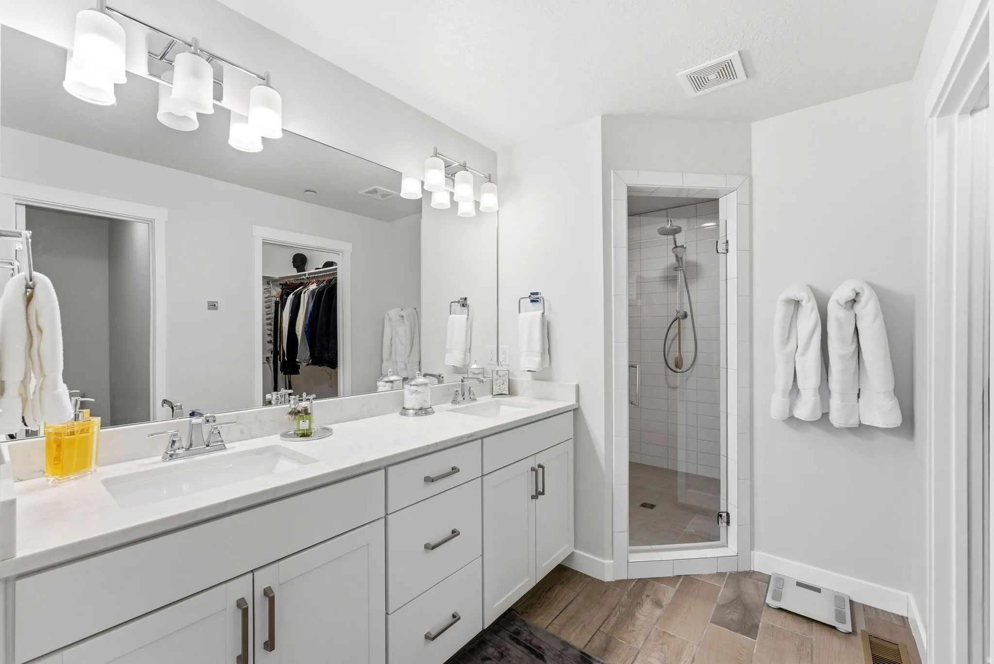 Bathroom with double vanity, a shower stall, light wood-style floors, and a spacious closet