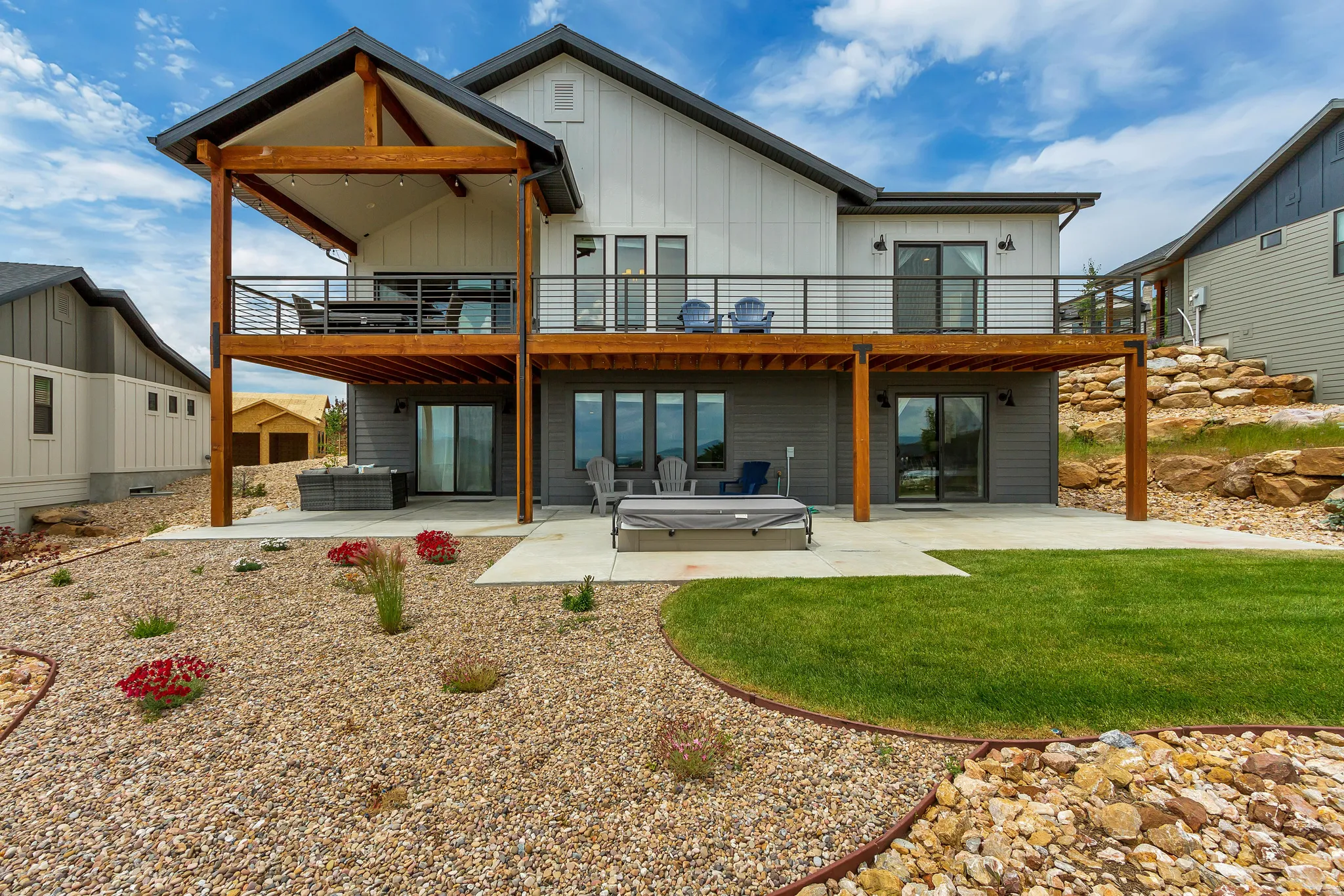 Back of house with a patio area, board and batten siding, a hot tub, a wooden deck, and outdoor seating