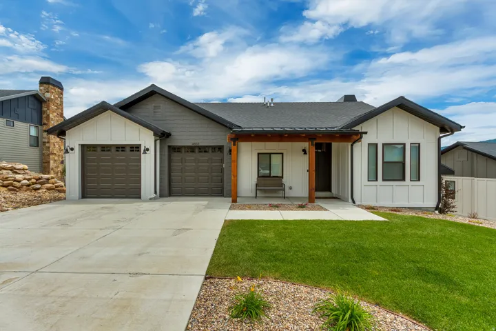 Modern inspired farmhouse with board and batten siding, a porch, a front yard, driveway, and a garage