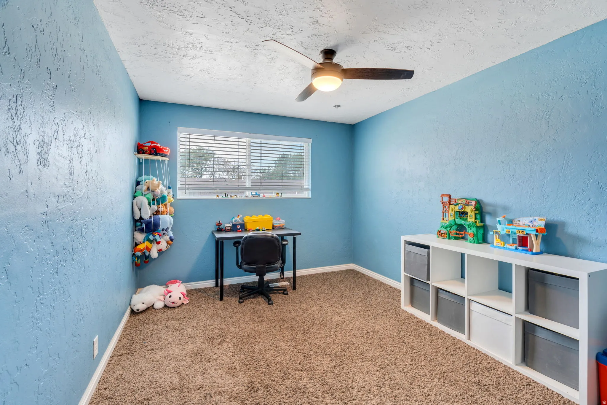 Home office with a textured wall, a ceiling fan, light carpet, and a textured ceiling