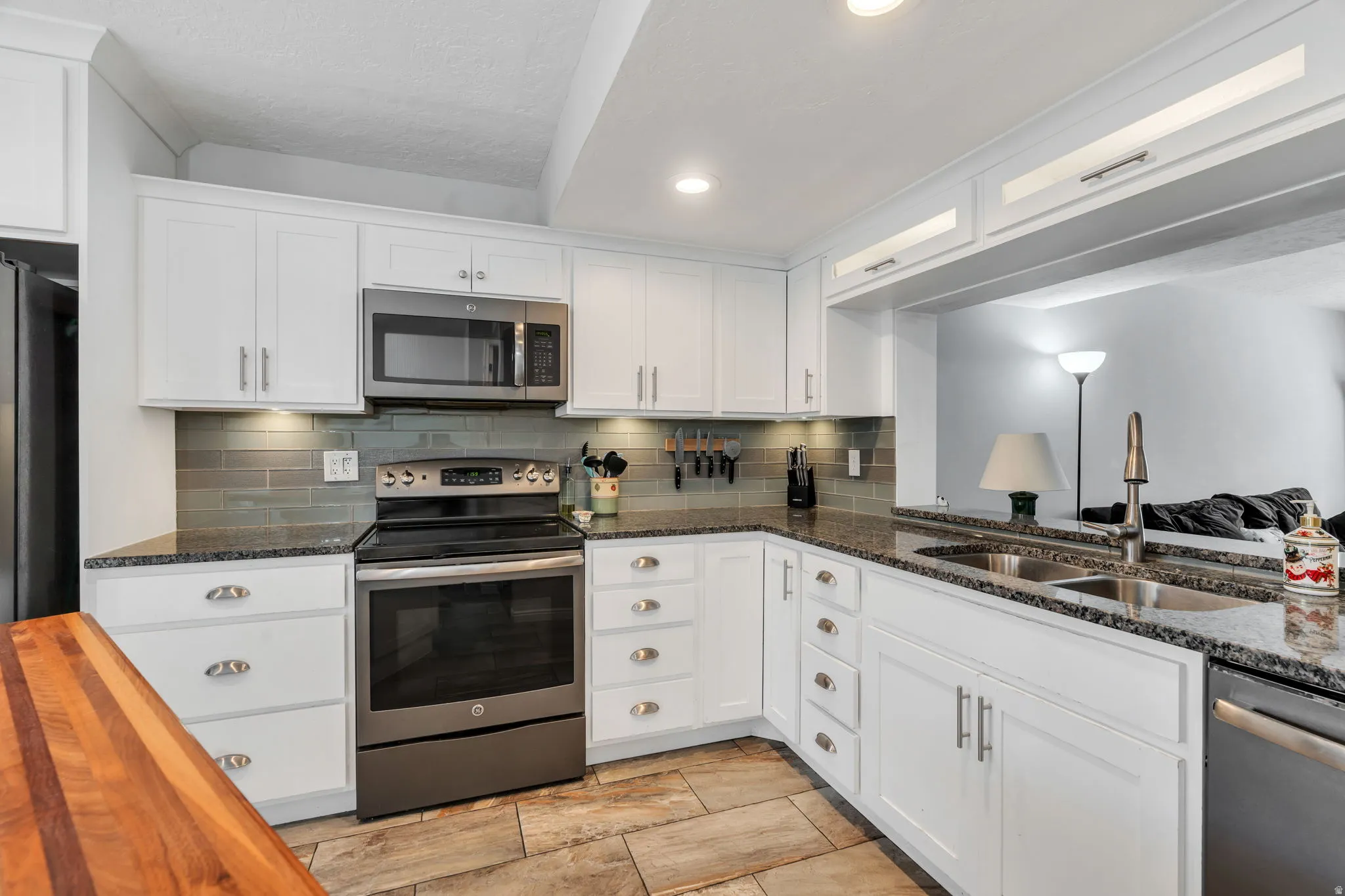 Kitchen with stainless steel appliances, dark stone countertops, white cabinets, decorative backsplash, and recessed lighting