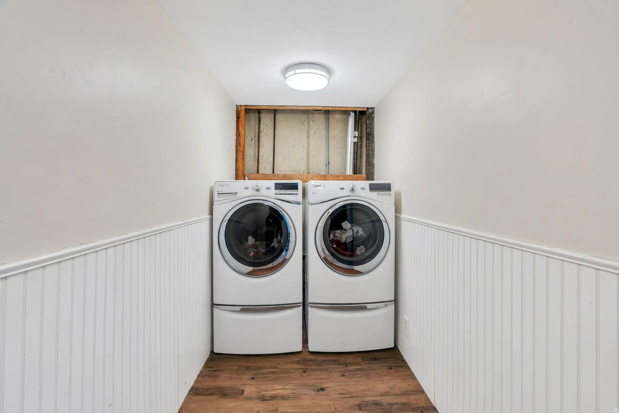 Laundry room featuring a wainscoted wall, dark wood finished floors, and washing machine and clothes dryer