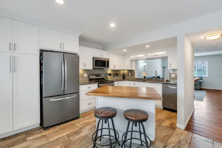 Kitchen featuring stainless steel appliances, butcher block countertops, white cabinets, a kitchen island, and a breakfast bar