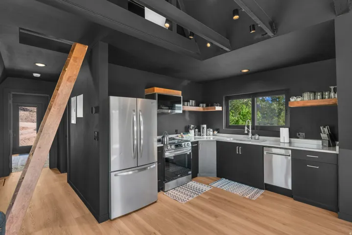 Kitchen featuring stainless steel appliances, dark cabinets, light countertops, open shelves, and light wood finished floors